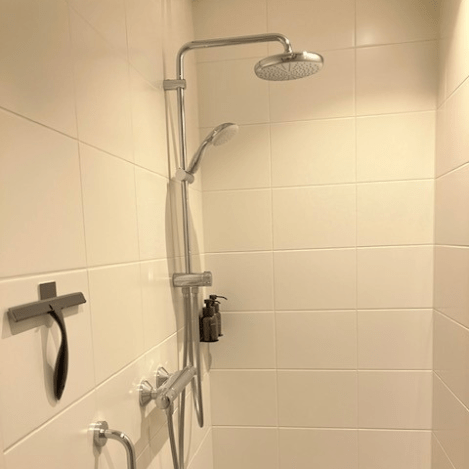 Een luxe inloopdouche met een grote regendouchekop en een handdouche, uitgevoerd in een minimalistisch design met witte tegels.