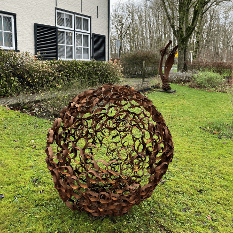 Een kunstzinnige metalen sculptuur met een bolvormig ontwerp, geplaatst in een groene tuin bij het verblijf.